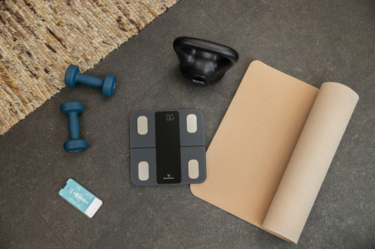 Sacoma slimme weegschaal met yogamat, kettlebell, dumbbells en de app op een telefoon
