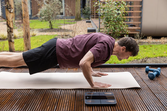 Man doet push-ups op een terras met een Sacoma weegschaal en dumbbells naast de mat